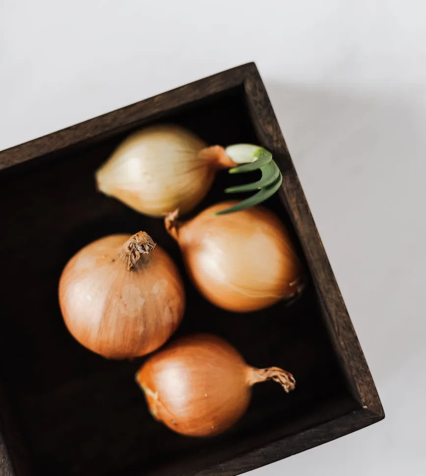Empat bawang bombai berkulit kuning keemasan di dalam kotak kayu gelap, satu di antaranya sudah bertunas hijau.