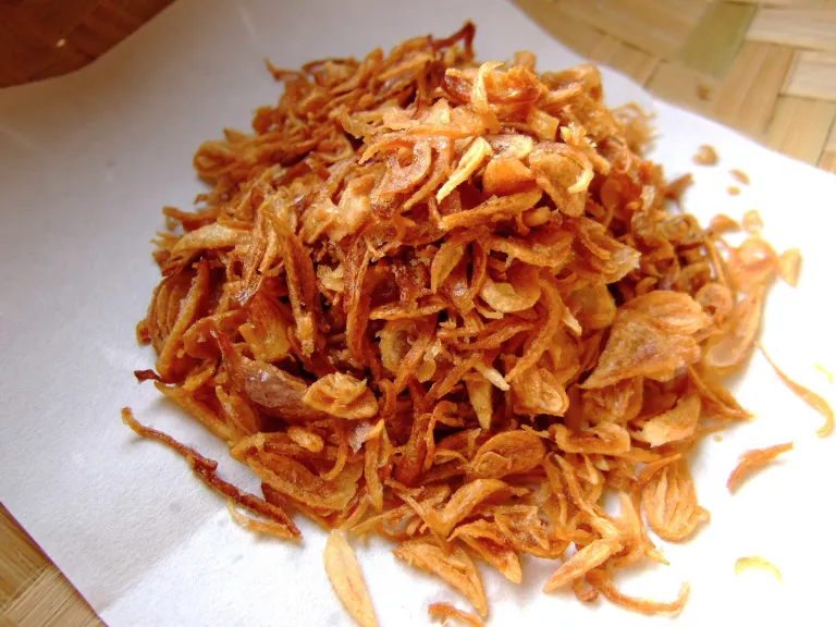 Setumpuk bawang goreng berwarna cokelat keemasan di atas tisu dapur.