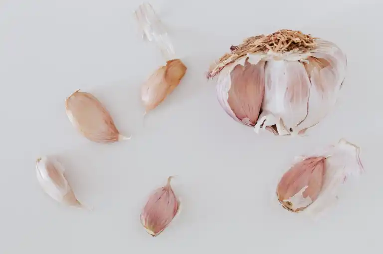Satu umbi bawang putih yang sudah terbuka di atas permukaan putih, dengan empat siung terlepas di sekitarnya.