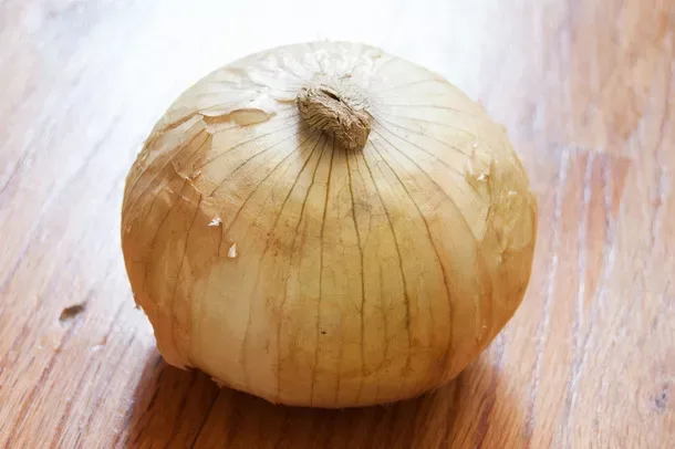 Satu bawang Sweet Onion berkulit kuning muda keemasan, berdiri di atas meja kayu.