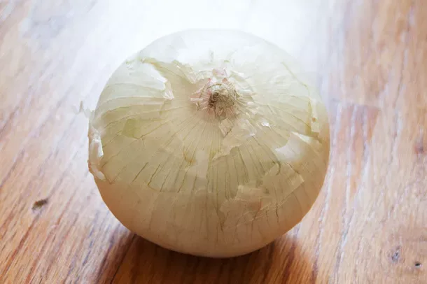 Satu White Onion berkulit putih kekuningan tipis, berdiri di atas meja kayu.